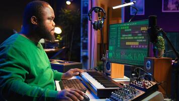 Musician playing piano keys and editing to improve sound quality of audio recordings in his home studio, putting on headset. Music producer uses midi controller to manipulate sounds. Camera B. photo
