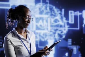 African american admin writes code on tablet to visualize artificial intelligence neural networks using augmented reality. High tech workspace supervisor runs AI script for information processing photo