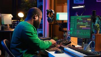 African american composer creating a new track for a project, using professional production pc interface in his home studio. Creative artist songwriter producing music with sound effects. Camera A. photo