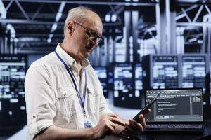 Elderly technician coding in high tech data center using javascript language. Certified specialist updating software on server rigs on laptop terminal, ensuring optimal performance and security photo