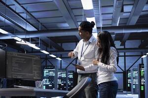 Programmers in data center running system diagnostic tests on PC and tablet to fix problems. IT specialists deploying and error checking utilities on devices to repair network issues in server racks photo
