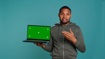 Smiling man holding isolated screen laptop, doing recommendation, talking with audience. Cheerful person pointing towards chroma key notebook, studio background, camera B photo