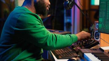 Skilled male composer producing new songs on his mixing console, operating on professional gear in home studio. Artist audio engineer twisting knobs to adjust sound levels on tracks. Camera A. photo