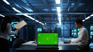 Focus on mockup laptop used by technician in data center in blurry background managing servers. Close up of chroma key notebook used by expert in server hub to ensure networks are secure, camera B photo