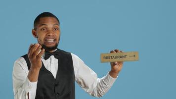 Doorman bellhop showing the restaurant direction with a hotel sign, holding an indicator to point guests to the amenities. Professional hotel concierge using a wall mark. Camera A. photo
