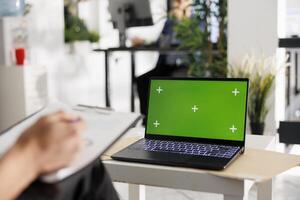 Laptop with chroma key green screen in coworking space for business presentation mock up. Corporate portable computer with blank display in modern green open space office photo