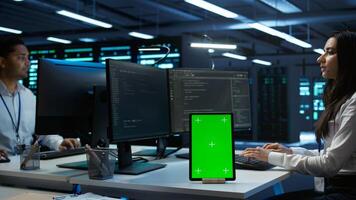 Software developer in data center monitoring security threats using mockup tablet. IT professional using green screen device, ensuring compliance with server room regulations, camera B photo