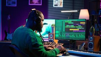 African american music producer twisting knobs on mixing console, produce tracks with sound effects. Artist composing songs in post production, operates on digital software in home studio. Camera A. photo