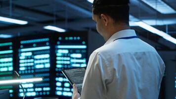 Data center engineer responsible for installation and repair of networking equipment solving tasks on device. IT professional doing maintenance on server room infrastructure using tablet, camera A photo
