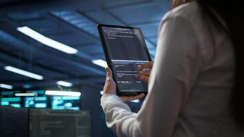 Data center software developer responsible for installation of networking equipment solving tasks on device. Close up of woman doing maintenance on server room infrastructure using tablet, camera B photo