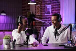 Team of smiling content creators hosting online show in living room studio, filming vlog using professional equipment. Vloggers discussing workflow for upcoming episode for streaming service photo