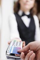 Close-up of elderly guy using credit card to make financial transaction at registration counter. Detailed shot showing contactless payment done at hotel front desk with guest and female receptionist. photo