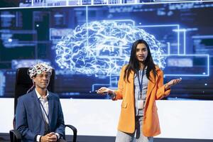 Portrait of IT experts talking at AI summit, sharing neural implants industry insights to audience. Engineers at artificial intelligence event presenting latest AI EEG headsets, doing demonstration photo