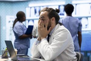 Frustrated and worried medic reading the diagnosis on test results, working under pressure to find the right treatment plan for recovery. Skilled doctor is stressed while checking hospital records. photo
