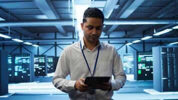 System administrator in data center managing and maintaining databases, ensuring data integrity, security and availability. IT worker updating server room supercomputers systems, camera B photo