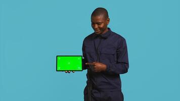 Portrait of happy security staff member showing isolated screen tablet. Joyous patrolling agent maintains secure environment, showcasing chroma key device, studio background, camera B photo