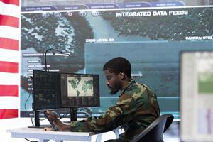 American military officer works in a high tech command post, managing national safety operations with the surveillance systems. Examining data for intelligence gathering. photo