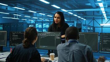 Manager overseeing server room, walking around with checklist on laptop, troubleshooting hardware and discussing with employees. Supervisor doing inspection in server hub, taking feedback from workers photo