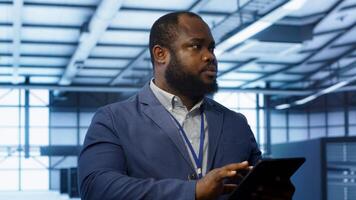 IT technician walking in data center, overseeing server operations using tablet. Expert ensuring optimal performance and data integrity in server hub using digital device, camera A photo