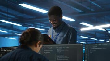 Manager overseeing team and doing system analysis of server farm supercomputers using tablet. Man supervising employees in data center housing storage infrastructure supporting critical IT workloads photo