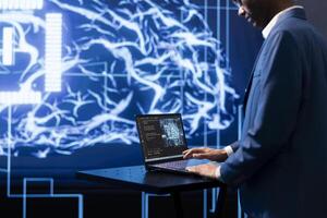 AI computer scientist using laptop device in high tech futuristic workspace. IT professional working on notebook to automatize tasks using artificial intelligence technology photo