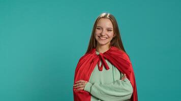Radiant woman grinning while portraying confident superhero wearing red cape, isolated over studio backdrop. Portrait of jolly heroic person posing as powerful hero character in costume, camera A photo