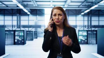 Technician in data center talking in phone call, doing yearly inspection. On field system administrator talking with manager in server hub during telephone call, monitoring servers, camera B photo