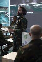 Army IT professional supervising data collecting activity from a big screen, processing strategic information to create a new map for field operations. Military defense program in control room. photo