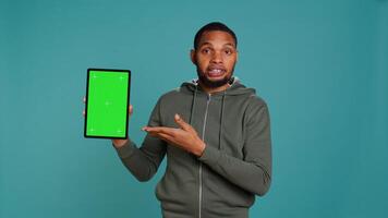 Joyous african american man holding isolated screen laptop, doing recommendation. Upbeat person pointing towards chroma key device, giving positive feedback, studio background, camera B photo