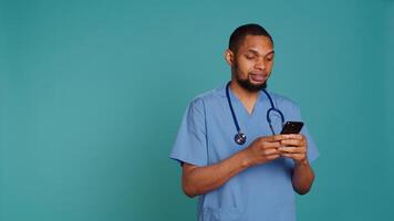 Male nurse using mobile phone to scroll on social media feed during hospital job shift break. Healthcare worker using smartphone to text friends, studio backdrop, camera B photo