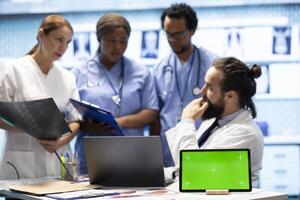 Diverse team of specialists examining radiography test scans with isolated screen in a meeting, reviewing x ray results at a treatment center. Professional staff ensuring disease prevention. photo