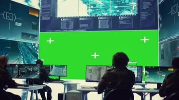 Team of IT military specialists working with a greenscreen on a big display, searching for real time data via reconnaissance CCTV system. Soldiers in power base transmitting information. Camera B. photo