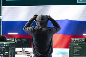 Russian hacker with a hood installing panic by misconception and manipulation, working in governmental cyber operations room. Impact of fake news and ideology propaganda in a hybrid war. photo