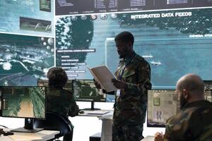Military secret service staff monitoring air traffic activity in control center, reviewing data from case files and big screen. Trooper collects intelligence from satellite reconnaissance system. photo