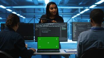 Supervisor in server hub managing diverse team of developers using green screen laptop looking for misconfigurations. Manager coordinating experts mending data center bugs with chroma key notebook photo