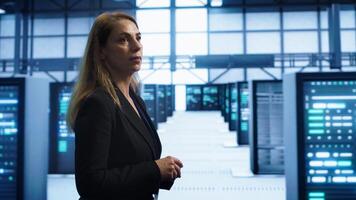 Engineer walking in data center workspace, monitoring systems to identify root cause of errors. Woman in server hub establishment doing diagnosis, looking for equipment bugs needing repairs, camera A photo