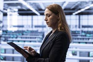 Data center software developer ensuring safety and security of database using tablet. Cybersecurity professional in server farm preventing unauthorized access posing risks for company photo