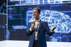 Cheerful engineer presenting how AI technologies can bring businesses increased productivity during conference. Jolly man using microphone to discuss about implementation of AI driven solutions photo