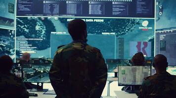 Staff sergeant monitoring satellite live imagery on a big screen, gathering information for future military operations. Army officer employs reconnaissance system in command post. Camera B. photo