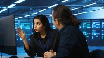 Programmers talking in high tech server hub, using PCs to analyze data. Colleagues examining infrastructure in data center, ensuring system integrity and security, doing brainstorming photo