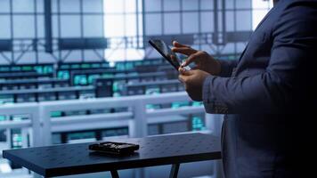 Technician in server hub workplace installing newly ordered storage unit, checking parameters with tablet. IT expert in data center holding device, replacing storage mainframes components, camera A photo
