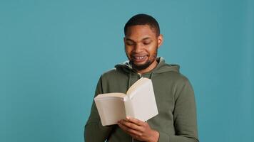 Man laughing while reading funny book, entertained by engrossing story. Joyful person having fun, being amused by literature novel during leisure time in studio background, camera A photo