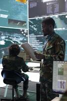 Army staff monitoring satellite surveillance activity on a big screen, troopers working in army command post. Recruit gathering real time data via radar reconnaissance system in control center. photo