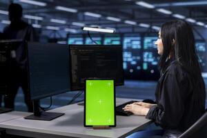 Admin in data center running system diagnostic tests using green screen tablet. Woman in server farm establishment deploying error checking utilities on mockup device to repair network issues photo