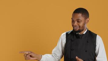 Waiter in professional uniform pointing at something to the left or right, creating a commercial ad for five star service oriented restaurant. Catering staff in hospitality industry. Camera A. photo