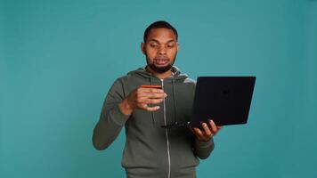 Happy man adding payment method on website using laptop, delighted to take advantage of promotions, studio background. Person thrilled to do internet shopping, typing credit card data, camera B photo