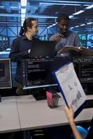 Man inspecting server hub infrastructure, reading paperwork from folder, talking with workers. Supervisor doing evaluation of data center facility workspace, verifying documents photo