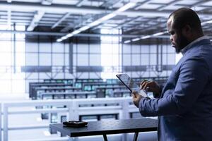 Engineer in data center using tablet to identify and solve technical issues related to data center infrastructure. IT professional managing, maintaining and securing server room environment photo