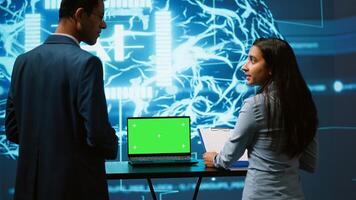 Startup coworkers brainstorming ways to use AI on chroma key notebook to improve data driven decisions. Technicians using mockup laptop to improve artificial intelligence tech, camera A photo