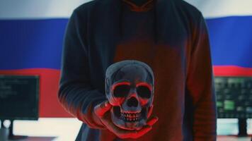 A maniacal russian hacker creating cyber threat alert by holding a skull as concept of cyber espionage and malicious code. Illustration warning of cyber security risks, evil harmful scam. Camera B. photo